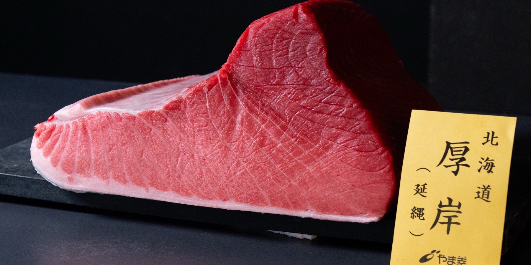 A whole block of Hokkaido bluefin on a black slate, with its Toyosu wholesaler's provenance card